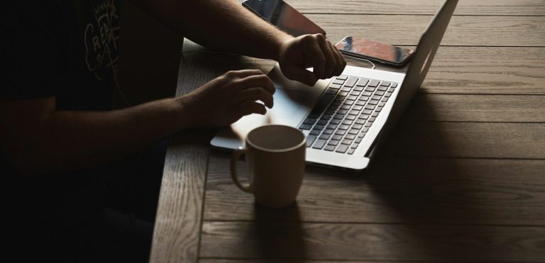 Starte jetzt dein Business Eine Hand tippt auf einer Laptop-Tastatur neben einer Kaffeetasse und einem Smartphone.